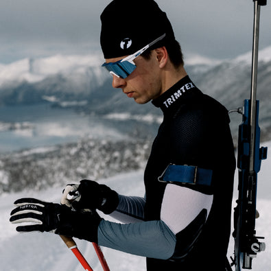Biathlete adjusting his ski pole straps. He is wearing Trimtex Biathlon Ace Racesuit and a Pulse Merino Cap.