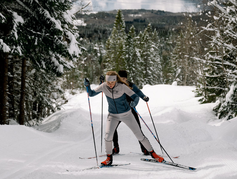 Two people cross country skiing. The woman is wearing Trimtex Ace skiing clothes and a Pulse Merino headband.