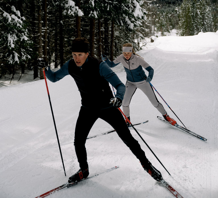 Man and woman are cross-country skiing. They are wearing Ace tracksuits.