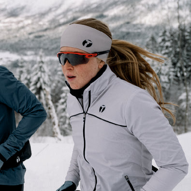Woman running in the snowy mountains, wearing Trimtex Instinct jacket and Pulse Merino headband.